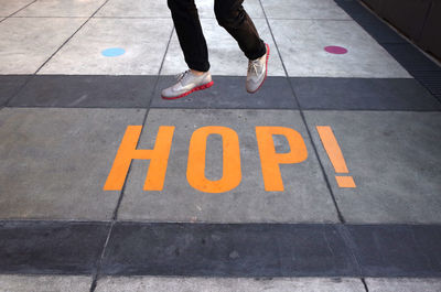 Low section of person jumping by yellow texts on footpath