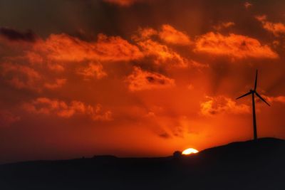 Low angle view of silhouette windmill against orange sky