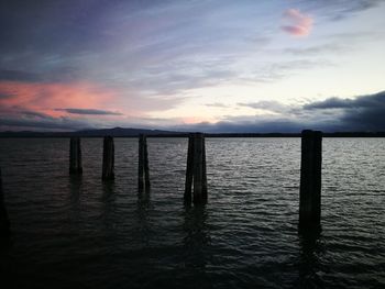 Wooden posts in sea against sky during sunset