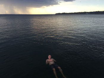 Shirtless man swimming in sea against sky during sunset
