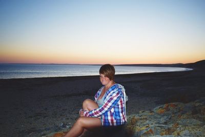 Portrait of woman sitting on beach against clear sky