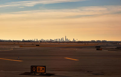 Empty runway in city against sky during sunset