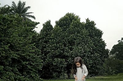 Girl standing by tree against sky