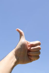 Low angle view of human hand against clear blue sky