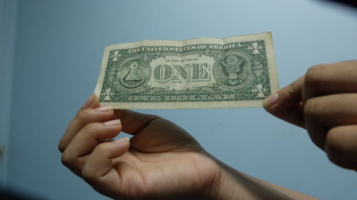 Cropped hands of woman holding paper currency against wall