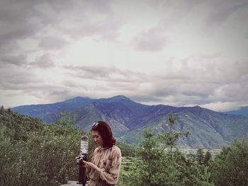 Woman using camera while standing against mountains