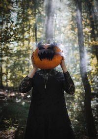 Woman wearing jack o lantern standing in forest