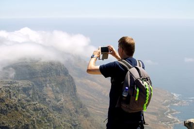 Rear view of man photographing standing against mountain range