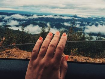 Cropped hand of woman touching window of car against mountain range