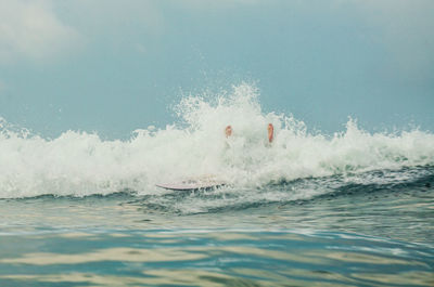 Low section of person surfing on sea against sky