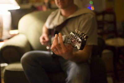 Midsection of man playing guitar while sitting on armchair at home