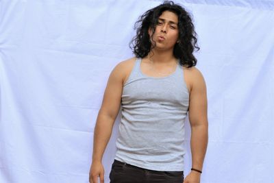 Portrait of young man with long hair standing against curtain