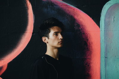 Portrait of young man looking away while standing against wall