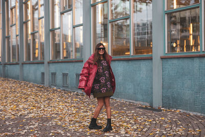 Portrait of young woman standing against building during autumn