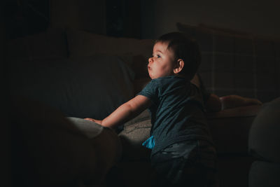 Rear view of baby boy standing by father sleeping on sofa at home