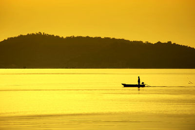 Silhouette man in sea against sky during sunset