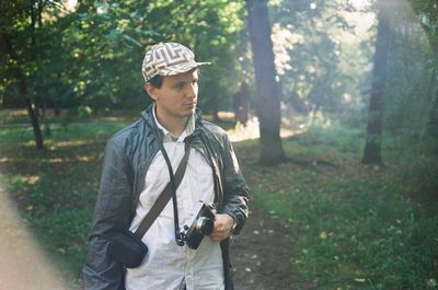 Young man standing with camera in forest