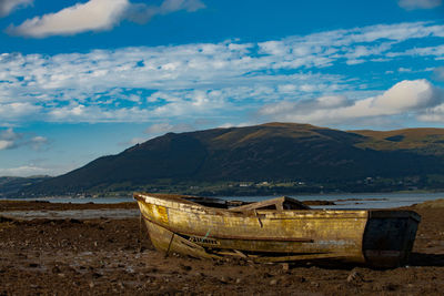 Boat moored on shore by mountains against sky