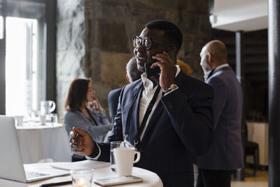 Businessman talking on smart phone while standing at table during seminar