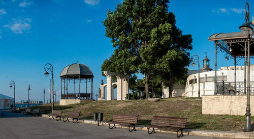 Empty park bench by building against blue sky