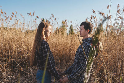 Young couple standing on field against sky