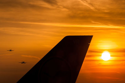 Cropped image of silhouette airplane flying against orange sky