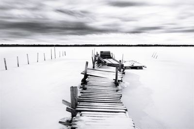 Wooden peer on snow in sea against sky