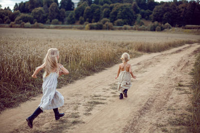 Two girls in long dresses running along the path to the field of dry wheat