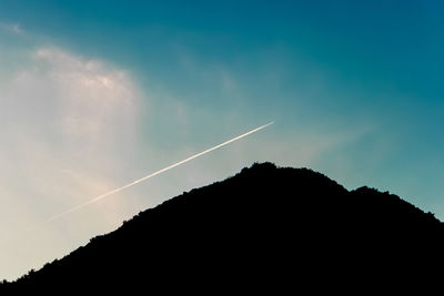 Low angle view of silhouette mountain against vapor trail in sky