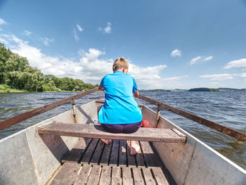 Young teenage boy rowing a rowboat or paddle boat on a lake with forest at bank. blue summer sky 