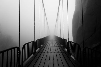 Empty footbridge in fog against sky