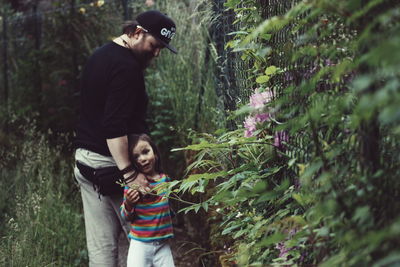 Father and daughter standing by plants growing at forest