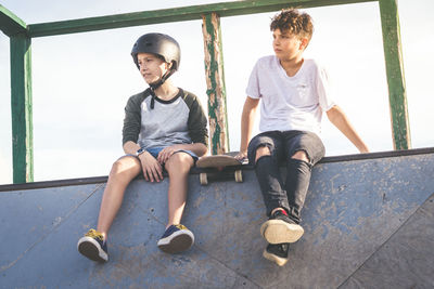 Low angle view of boys sitting on wall against sky