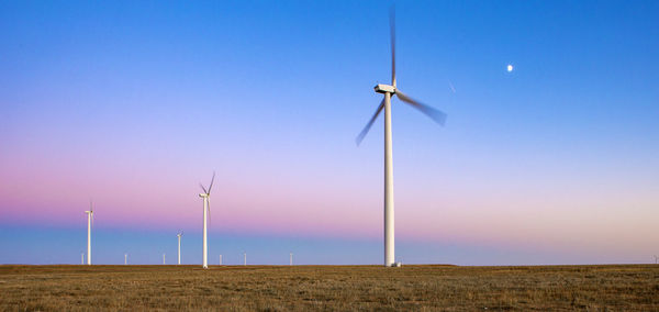 Wind turbines in field against blue sky at dusk