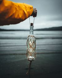 Close-up of hand holding illuminated bottle at beach