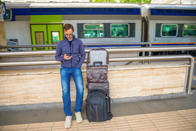 Full length of man using mobile while standing at railroad station platform