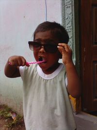 Boy in sunglasses brushing teeth outside door