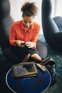 High angle view of mid adult businesswoman using mobile phone while sitting on chair at office cafeteria