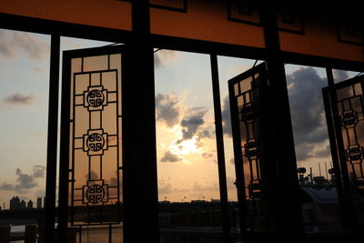 Silhouette buildings seen through window during sunset