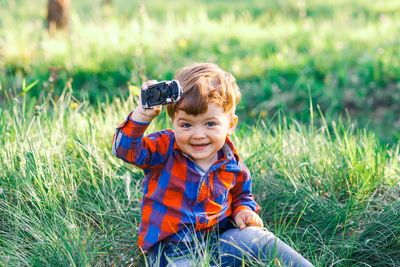 Portrait of boy holding toy car while sitting on field