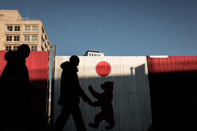 Silhouette people standing by building against sky