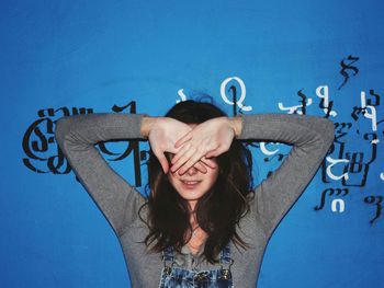 Teenage girl covering face with hands standing against wall