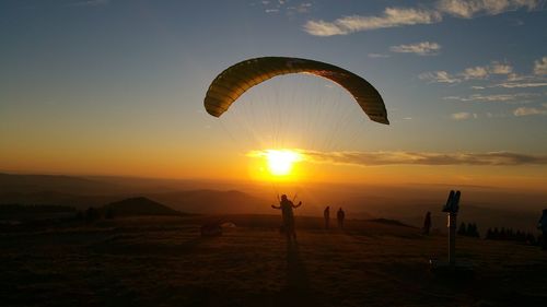 Person paragliding on mountain against sky during sunset