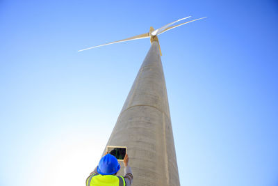 Low angle view of technician taking picture with a tablet of wind turbine