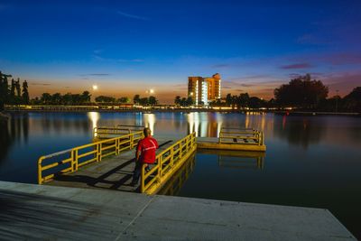 River by illuminated city against sky at sunset