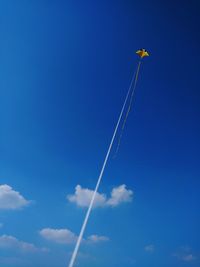 Low angle view of vapor trail and kite in blue sky