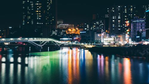 Illuminated buildings by river against sky at night