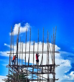 Low angle view of men working at construction site against blue sky