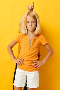 Young woman standing against yellow background