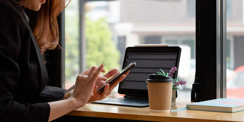 Midsection of woman holding mobile phone while standing on table
